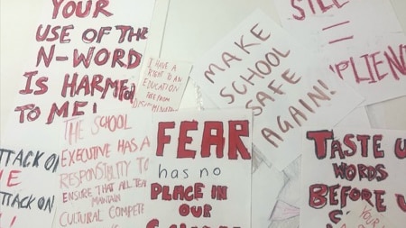 Signs held by students during a protest, including 'make school safe again' and 'fear has no place in our school'.