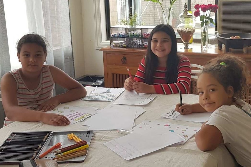 Four young girls sit around a dining room table writing letters.