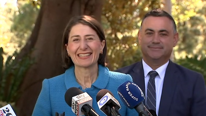 A man and a woman standing in front of media microphones.