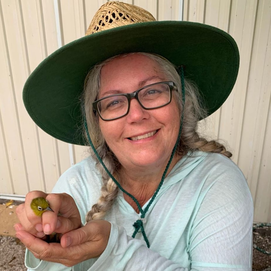 Woman holding a small bird, wearing wide-brimmed hat