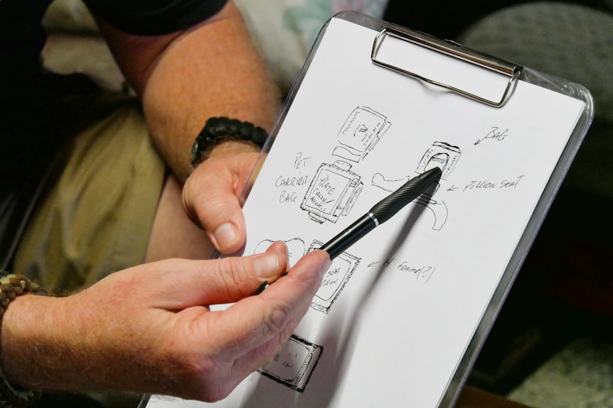 Man holds clipboard and points to hand drawn sketches with pen.