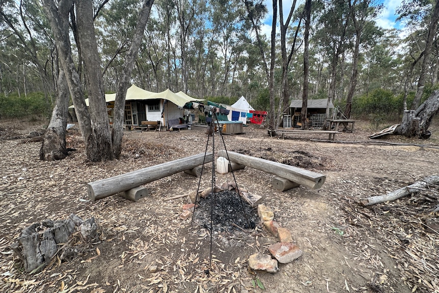 A campfire setup in front of tents and temporary buildings on a bush block