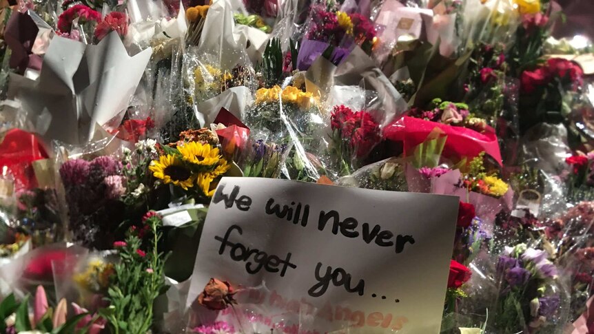 A large mass of flowers with a sign saying "we will never forget you" in the middle
