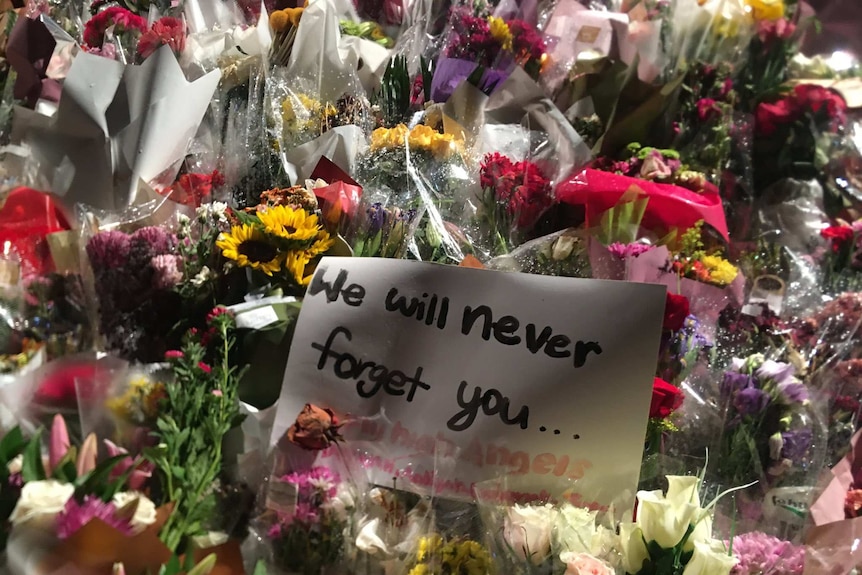 A large mass of flowers with a sign saying "we will never forget you" in the middle