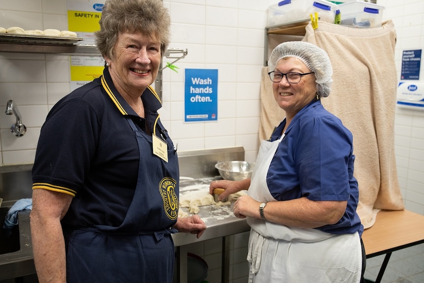 Two ladies making scones with a sign to "wash hands often" in the background.