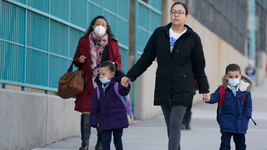 Children and their caregivers arrive for school while wearing face masks