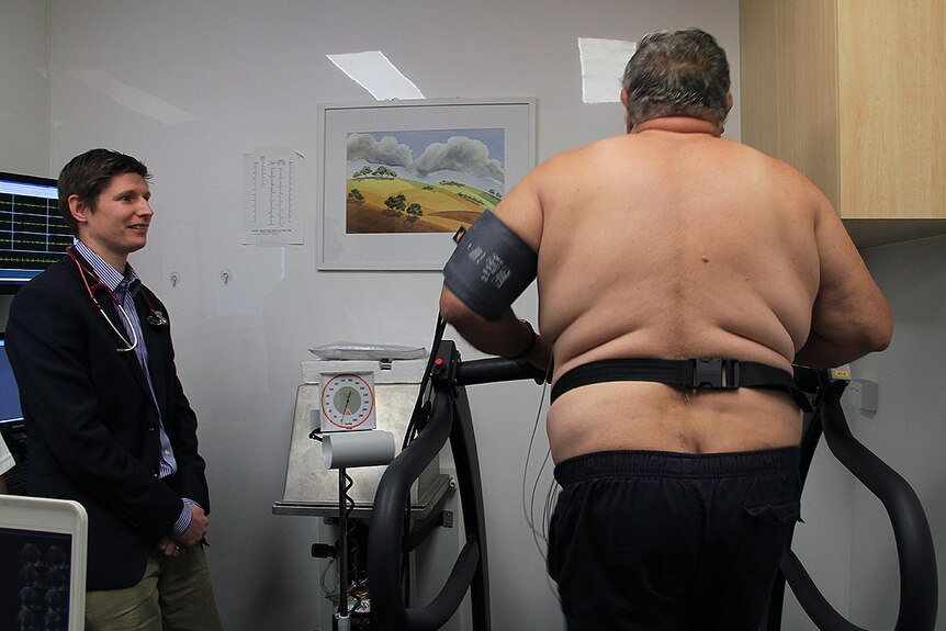 A man runs on a treadmill while a doctor watches on