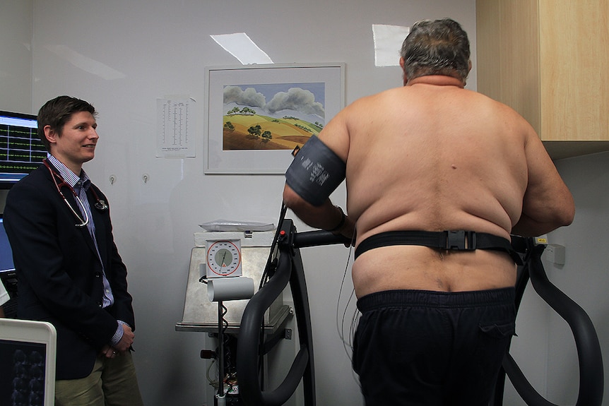 A man runs on a treadmill while a doctor watches on