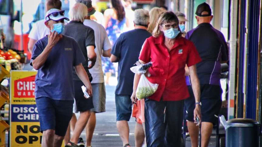 People walk down a suburban shopping strip wearing surgical masks.