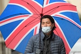 A man wearing a face mask and holding an umbrella with the Union Jack on it waits outside 10 Downing Street.