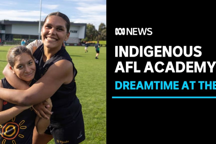 Indigenous AFL Academy, Dreamtime at the G: Two girls hugging on the field in front of people in the background.