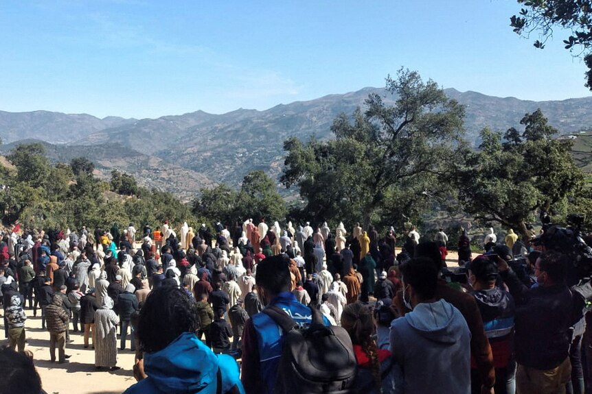 View of dozens of people gathering on a hill, in front of mountains