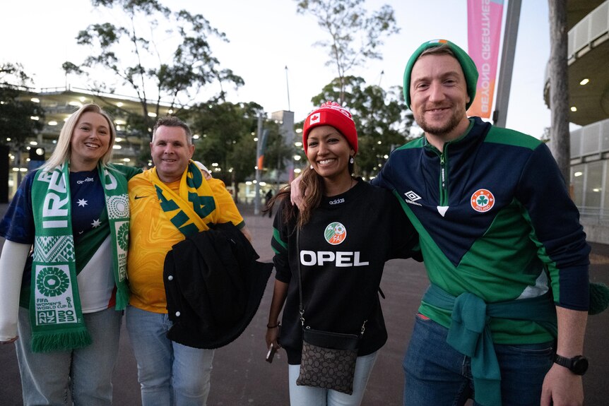 Four people dressed in Ireland and Australia football gear smile for the camera.