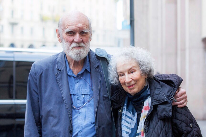 An elderly man and woman standing on the street, wearing jackets
