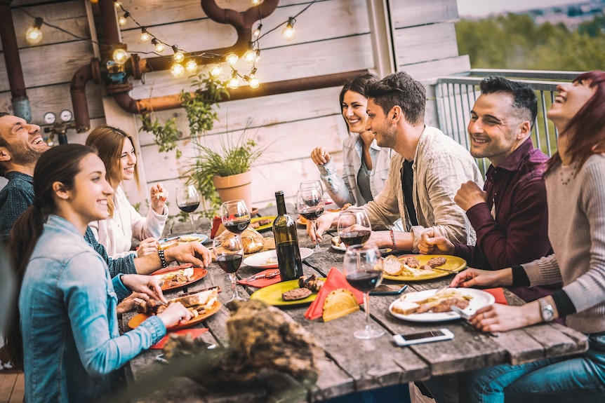 A group of young people enjoying an evening outside with wine and food