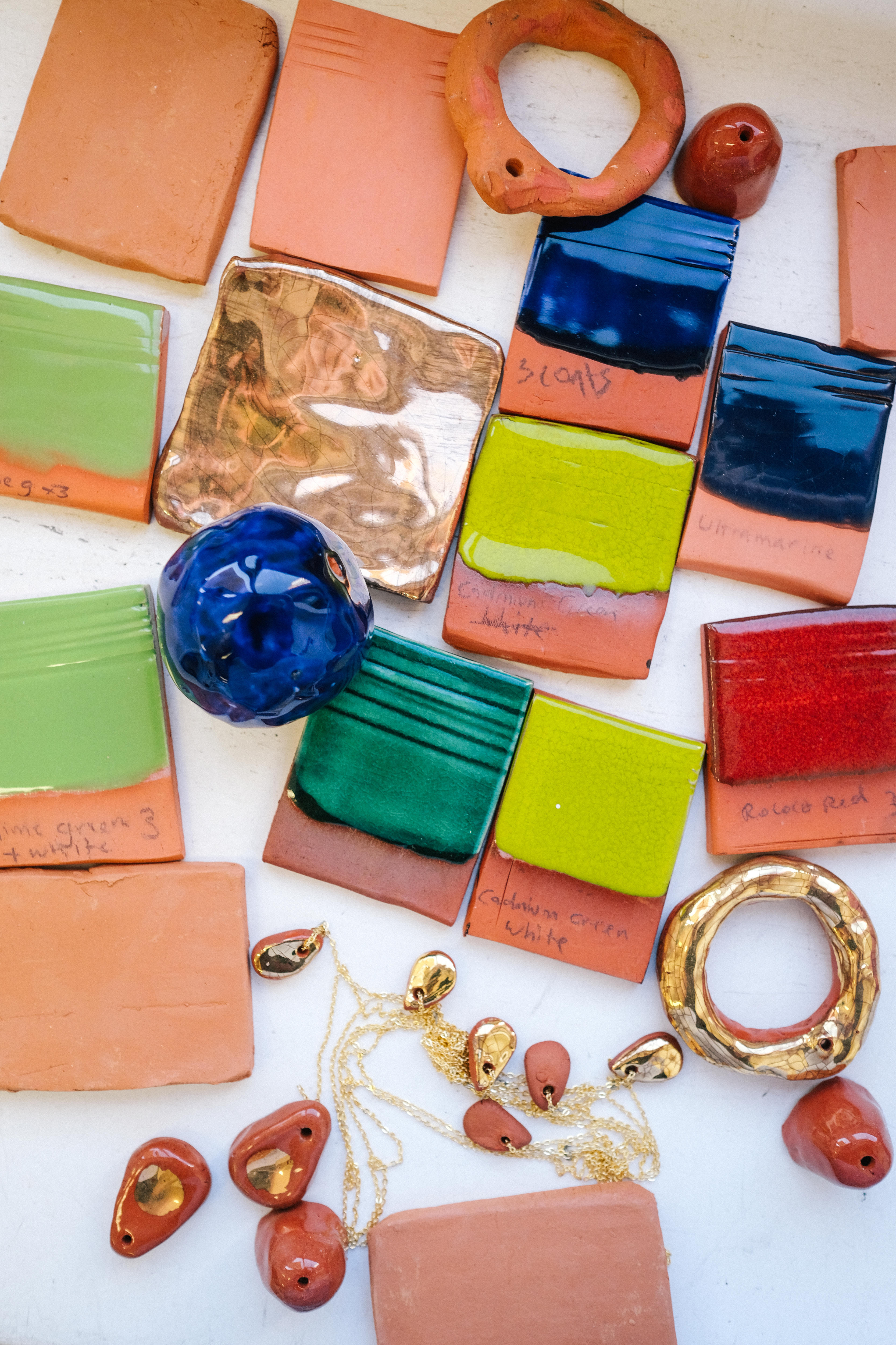 Close up, overhead image of test pieces of ceramics — squares of different colours, and gold glazed clay shapes.