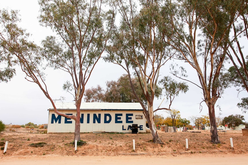 A row of trees stand in front of an old building with Menindee Lake painted on the side