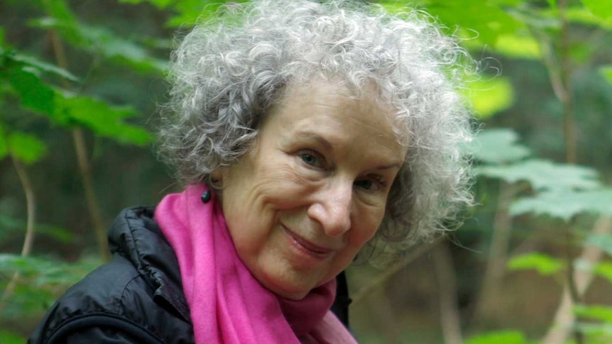 Author Margaret Atwood standing in a forest smiling and looking at the camera.