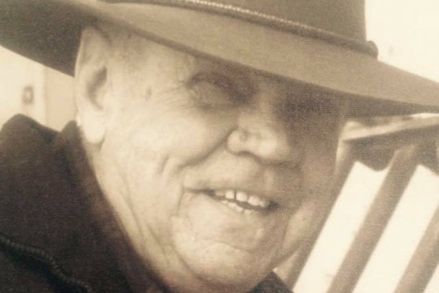An older man wearing an akubra smiles as he looks at the camera.