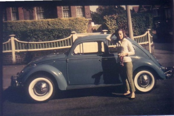 A woman stands in front of a blue VW Beetle.