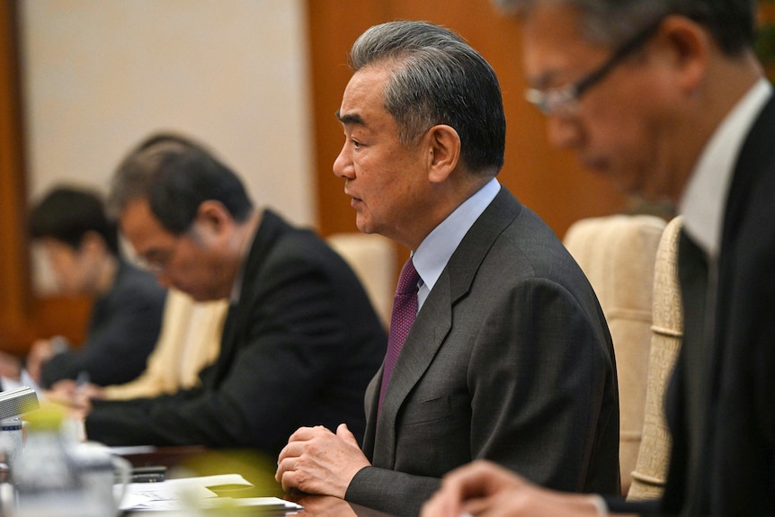 China's Foreign Minister Wang Yi sits and talks at a table with officials next to him during a meeting.