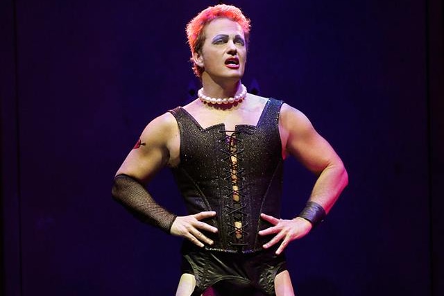 Craig McLachlan stands on stage in a black corset and tights in costume as Frank-N-Furter.