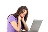 A woman sits at her computer holding her head in her hands and looking frustrated.
