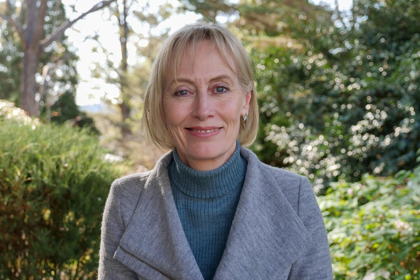 A woman stands centre frame looking out from a green garden. 