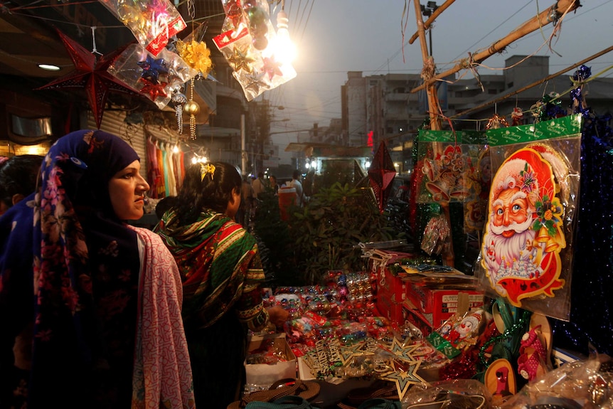 A Santa Claus decoration sticker hangs on a stall where women go through various items to buy for Christmas celebrations in Karachi, Pakistan.