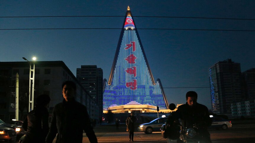 People cross the street as a propaganda message is displayed on the facade of the pyramid-shaped Ryugyong Hotel in Pyongyang.