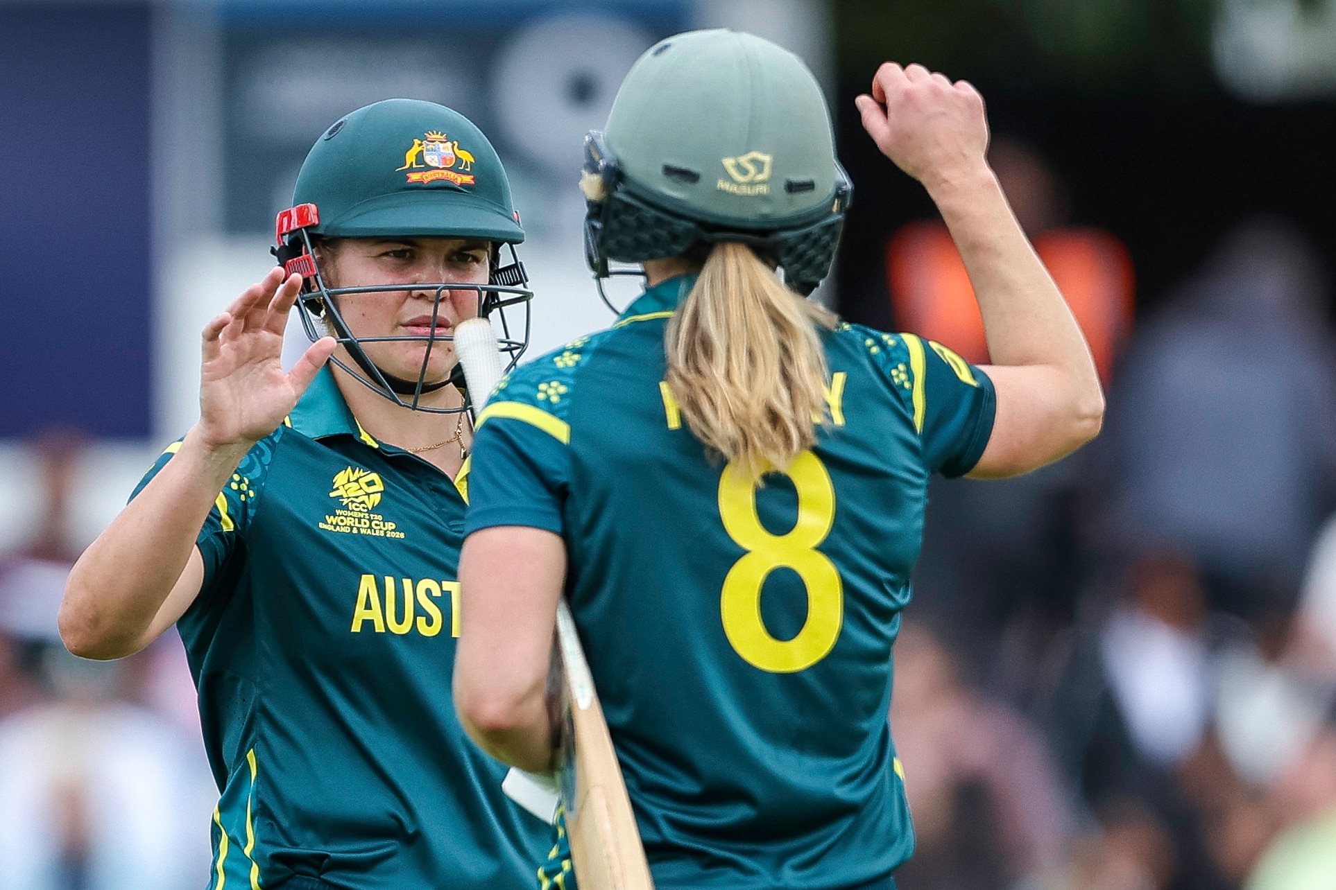 Two women cricket players on the pitch, both wearing helmets