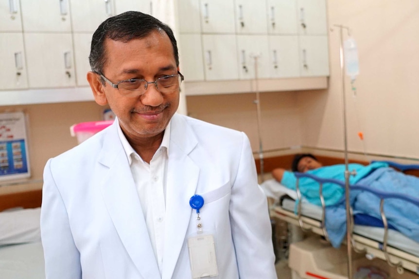 Gastroenterologist Murdani Abdullah, wearing a white coat, stands in front of a patient lying in a bed.