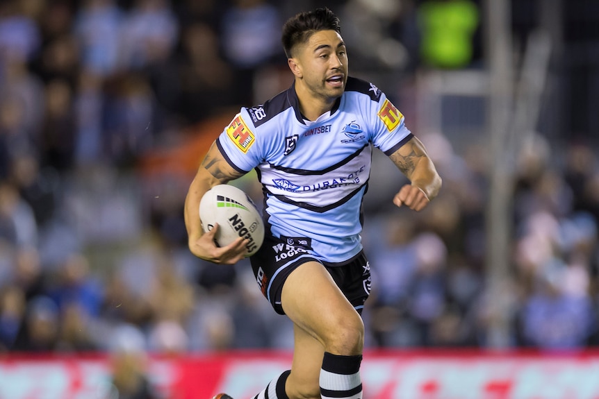 A male NRL player runs with the ball in his right hand.