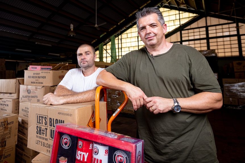 Luke Caridi and Martin Brady stand in a warehouse filed with boxes of fireworks stock.