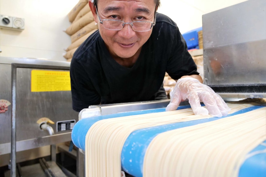 Shing Hee Ting making noodles in his backyard shed. The noodles have just been fed through a cutter