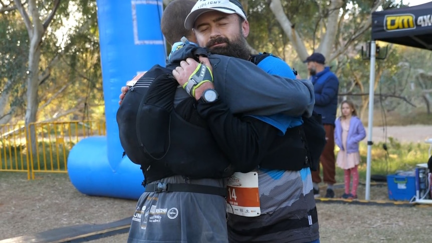 man dressed in running gear hugs another man at the finish line of a marathon