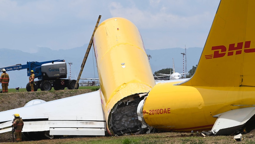 A large cargo plane sits on grass, with its tail section broken off, exposing cargo inside.