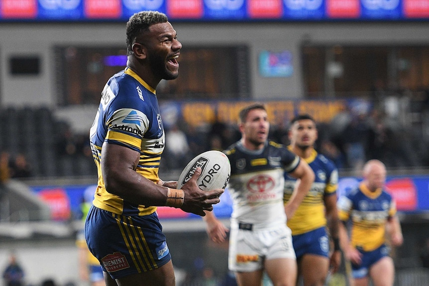 A Parramatta Eels NRL player holds the ball in his hands as he smiles after scoring a try against the North Queensland Cowboys.