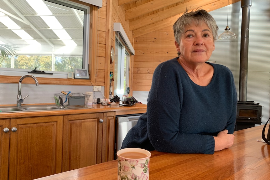 A middle-aged white woman with short grey hair. She is standing in the kitchen, looking into the distance