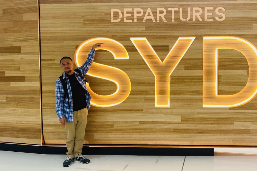 一名男子站在悉尼机场的出发标志旁