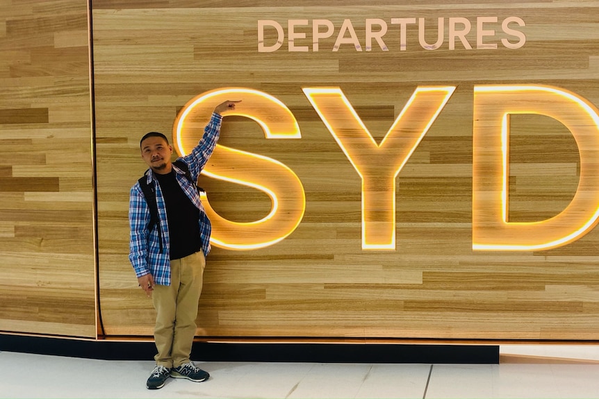 A man stands pointing to the departures sign at Sydney airport