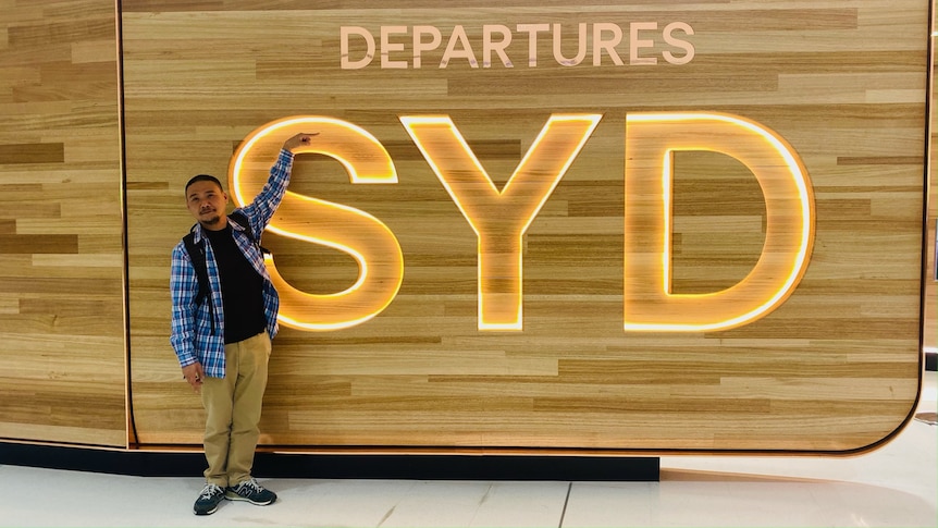 A man stands pointing to the departures sign at Sydney airport