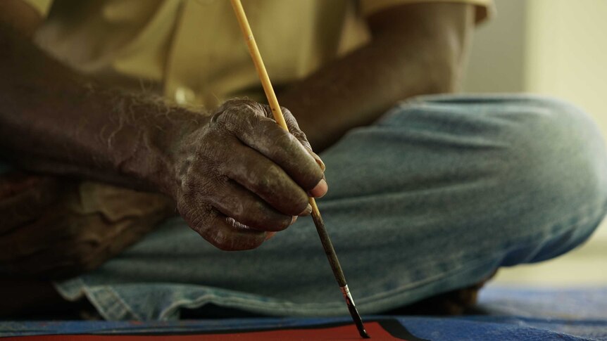 An Indigenous man's hand holds a paintbrush