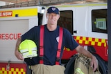Glen Saville holds his helmet and stands in front of a fire truck.