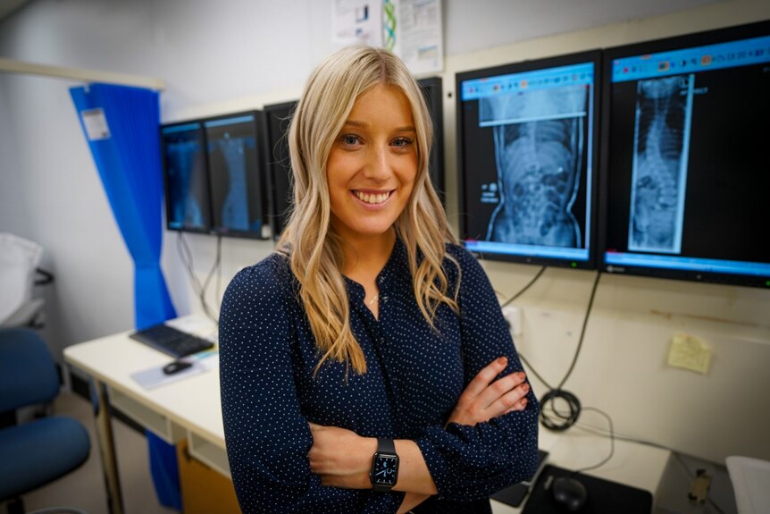 A woman with blonde hair in front of screens with X-rays on them