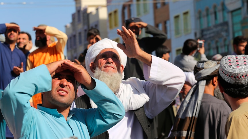 People look up at a dead body hanged by the Taliban from a crane in the main square of Herat