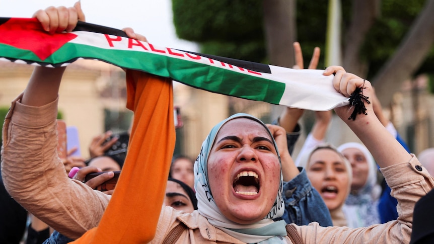 A woman yelling in a protest holding Palestinian sash.