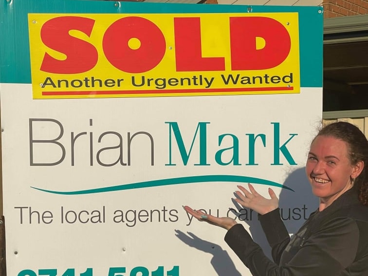 a woman smiling infront of a SOLD sign on a house