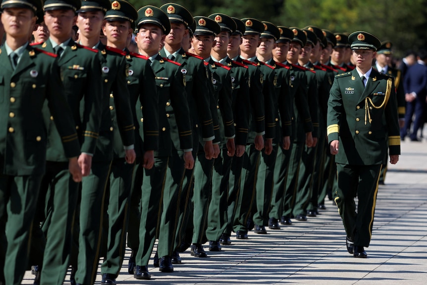 Chinese paramilitary police officers march in a straight line while wearing green dress uniforms.