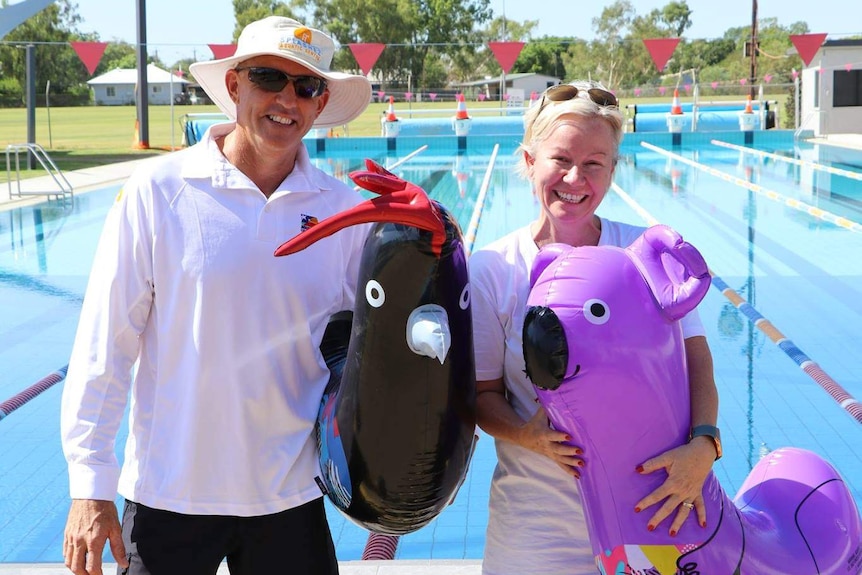 A man and woman holding pool toys in front of a large pool